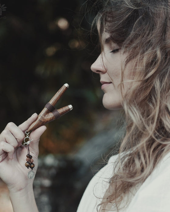 A serene woman holds a high-quality wooden kuripe blowpipe, used as a hape snuff applicator. The kuripe, doubling as a necklace with detailed charms, represents both a shamanic tool and a unique gift.