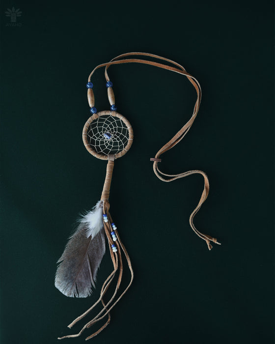 Tiny handcrafted dream catcher pendant on a leather cord, resting on a bed of dried lavender and crystals