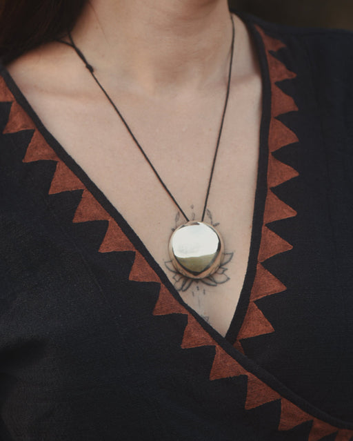 Necklace with a round pendant worn by a person in a black and brown patterned garment.
