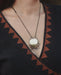 Necklace with a round pendant worn by a person in a black and brown patterned garment.