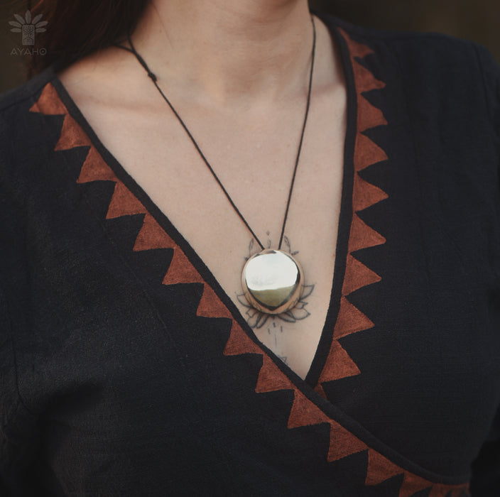 Necklace with a round pendant worn by a person in a black and brown patterned garment.