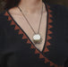 Necklace with a round pendant worn by a person in a black and brown patterned garment.
