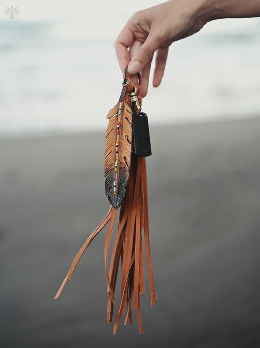 Delicate pheasant feather amulet with copper wire wrapping, suspended from a suede cord over a smudging bowl.
