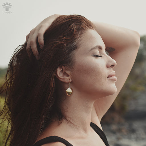 Bronze earrings with symbolic engravings and reflective mirrors, placed beside sage and crystals.