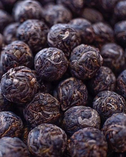 Hand-rolled pu-erh tea balls unfurling in glass teapot, releasing smoky aroma with earthy aged notes