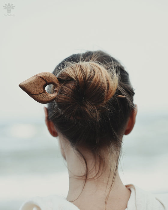 Lightweight acacia wood hair clip with a tapered leaf shape, photographed in sunlight to showcase its warm honey-toned finish