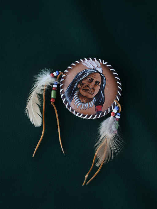 Close-up of a natural pheasant feather brooch with leather wrapping and brass details, pinned to a textured linen jacket.