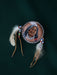 Close-up of a natural pheasant feather brooch with leather wrapping and brass details, pinned to a textured linen jacket.