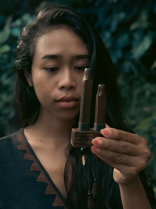 Person holding a wooden bow and arrow against a dark, leafy background