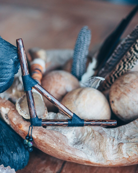 Decorative item with a metallic rod and blue cord on a wooden surface with feathers and stones.