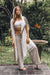 Woman in a white top and beige pants with a long white shawl standing outdoors.