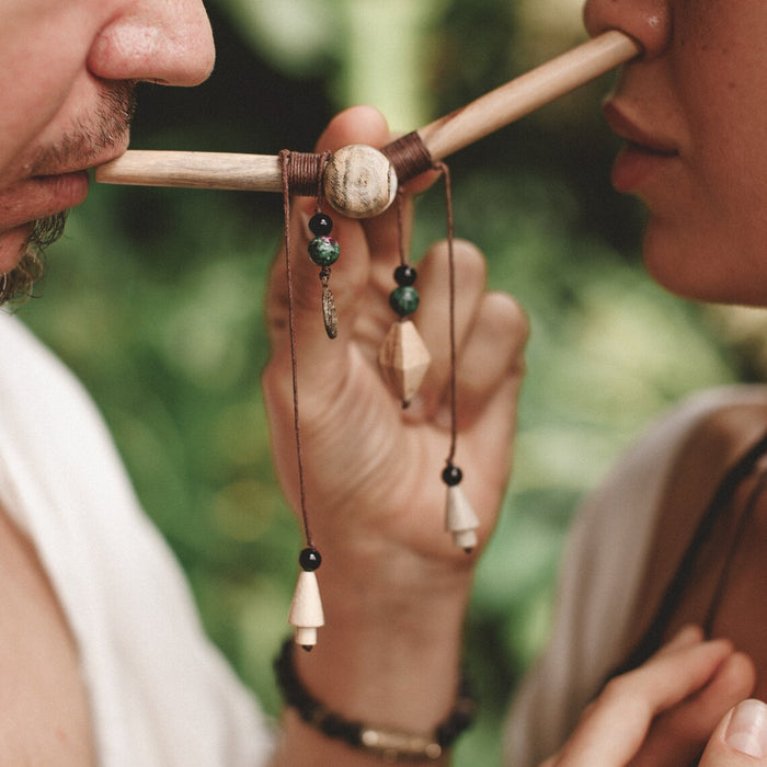 Two people holding a wooden pipe with beads against a blurred natural background