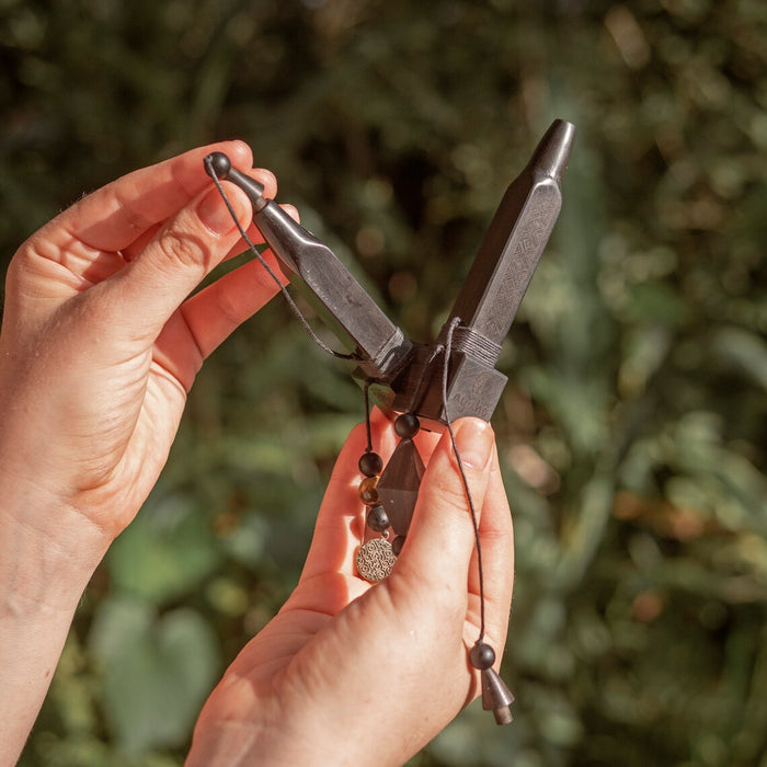 Hand holding a pair of pliers with beads against a blurred green background