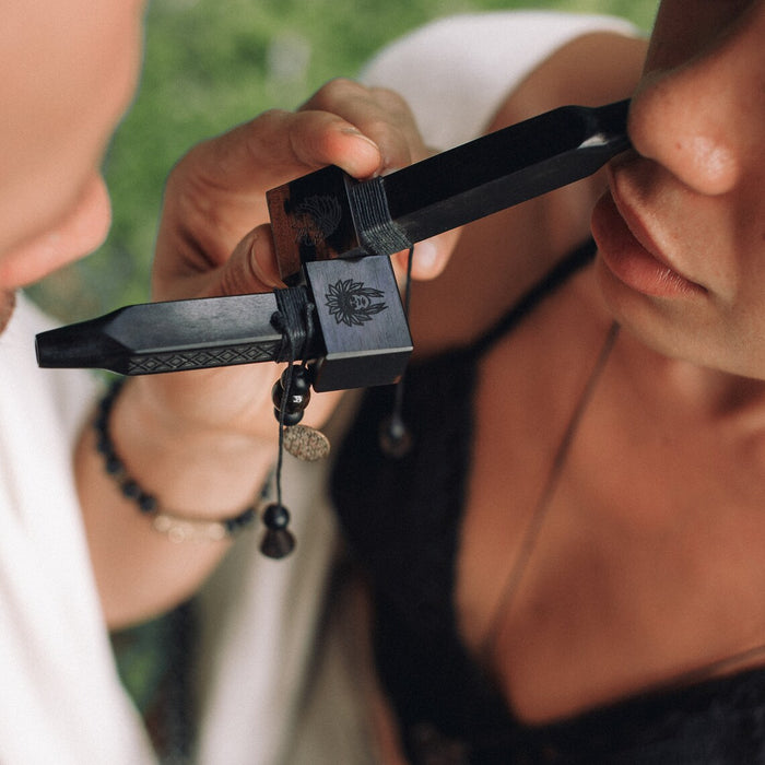 Two people holding a black object with a logo between their faces outdoors.
