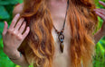 Person with long red hair and a necklace against a blurred green background