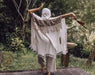 Person draped in a white shawl with fringe, standing in a natural setting.