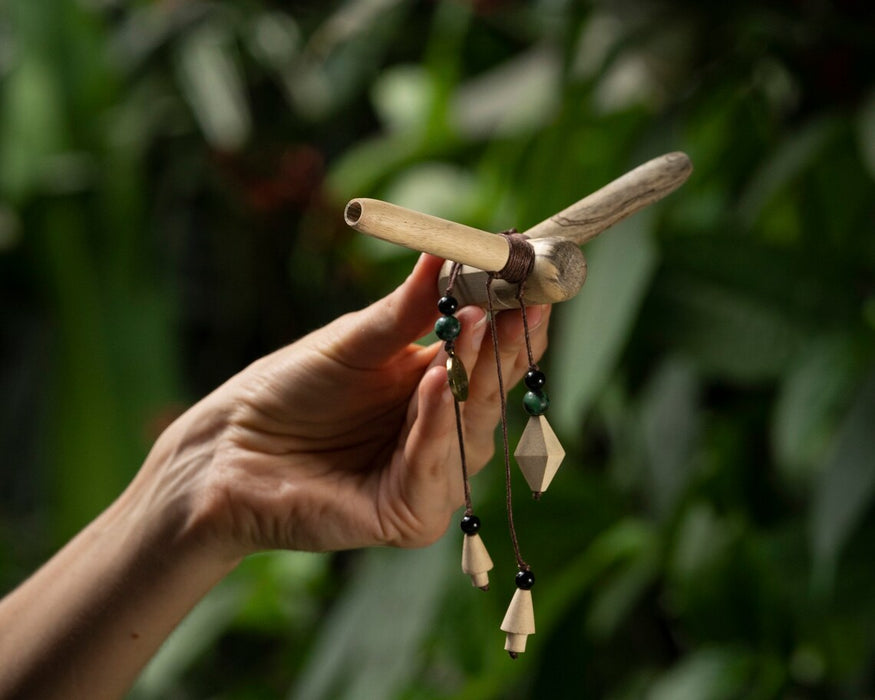 Hand holding a wooden and bead ornament against a blurred green background