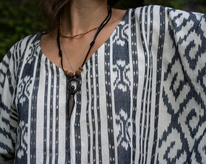 Person wearing a patterned shirt with a necklace featuring a black pendant.