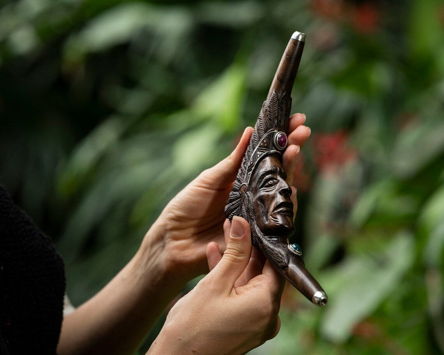 Hand holding a decorative smoking pipe with intricate carvings against a blurred green background