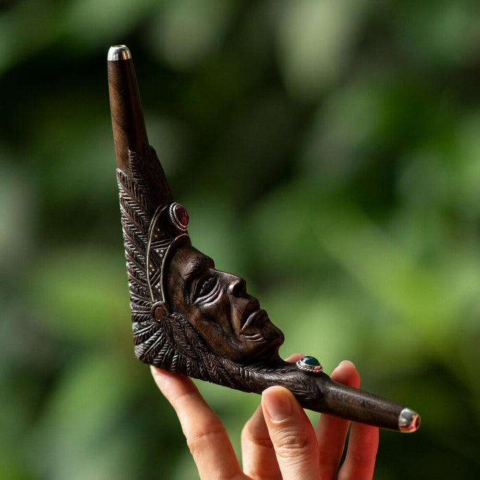 Decorative smoking pipe with face design held by a hand against a blurred green background