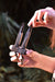 Person holding a black metal tool against a blurred natural background