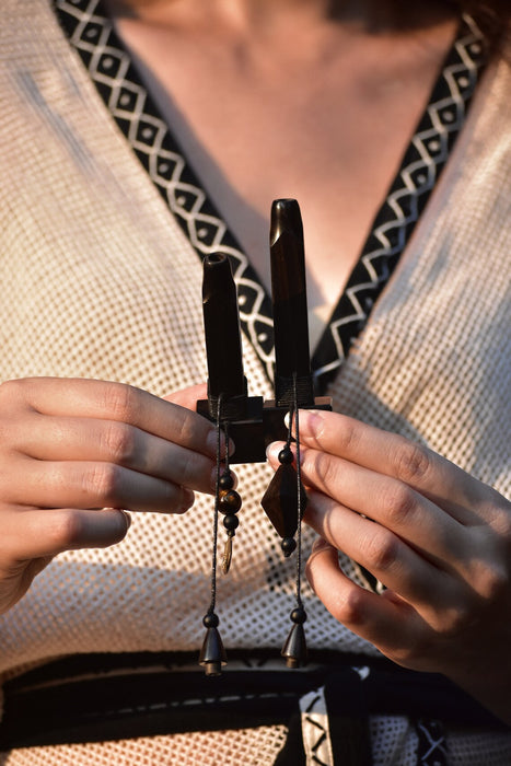 Person holding a pair of black pliers with small objects, wearing a patterned garment.