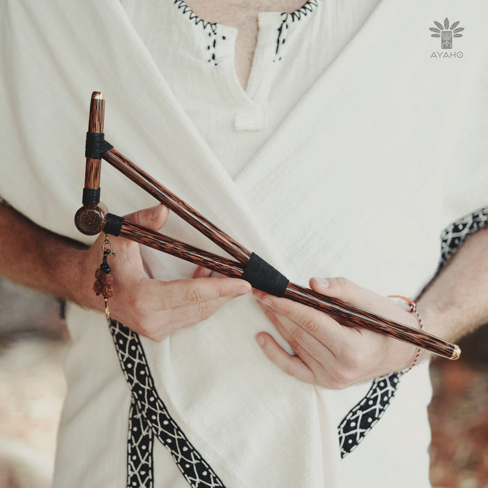 Person holding a set of wooden sticks with black bands, wearing a white garment with black patterns.