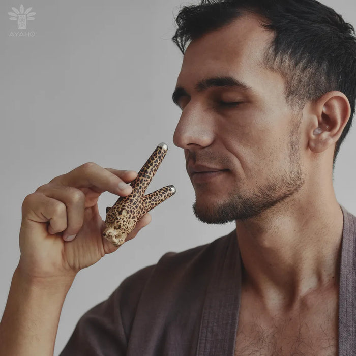 Man holding a small leopard print object close to his face against a neutral background