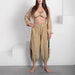 Woman wearing a beige outfit with long sleeves and high-waisted pants against a white background