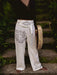 Person wearing white pants with tribal designs and a belt, holding a gong outdoors.