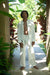 Man in white outfit standing in a tropical setting with greenery
