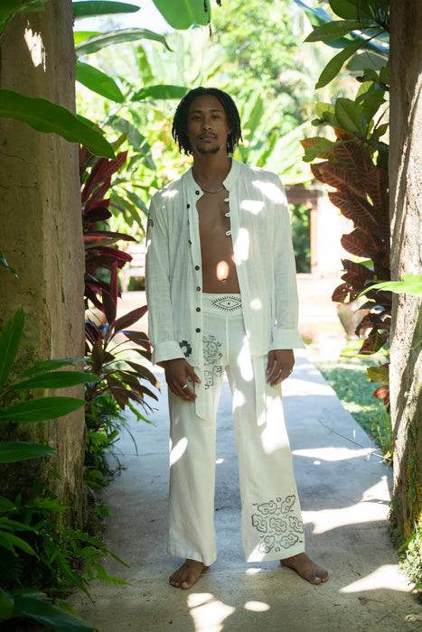 Man in white outfit standing in a tropical setting with greenery