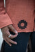 Person wearing a red garment with a black geometric design, holding their hand to their waist.
