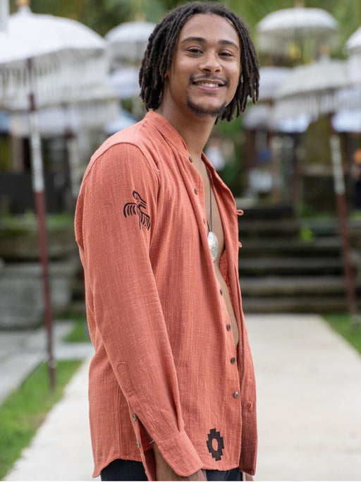 Man wearing a peach-colored shirt with patterns, standing outdoors.