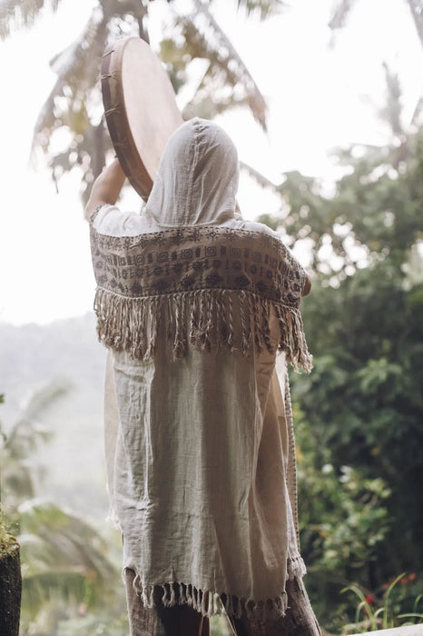 Person wearing a light-colored dress with a fringed shawl in a natural setting