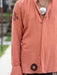 Person wearing a peach-colored shirt with black patterns, standing outdoors.
