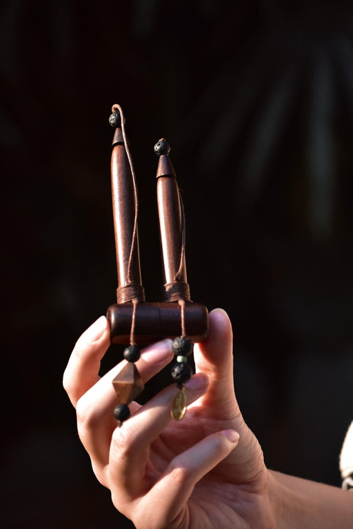 Hand holding a pair of intricately designed wooden tools against a dark background