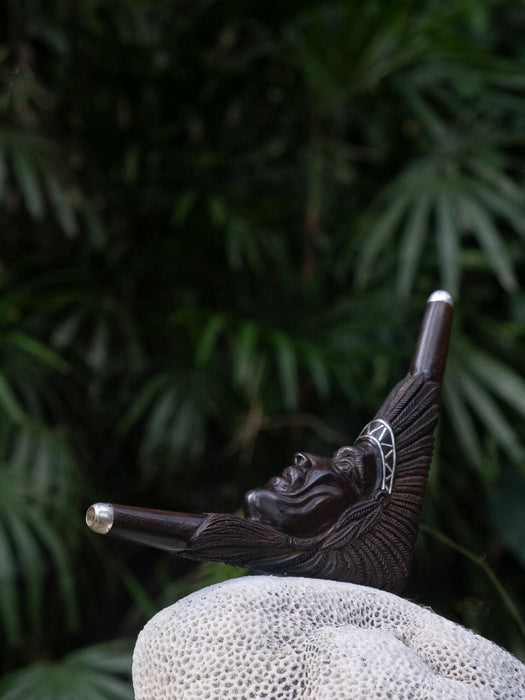 Wooden pipe with a face design on a textured surface with green foliage in the background