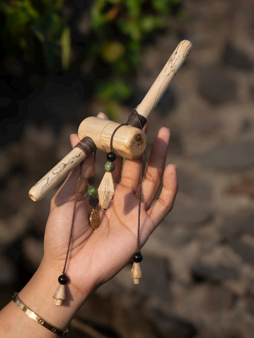 Hand holding a decorative item made of sticks and beads against a blurred natural background