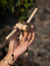 Hand holding a decorative item made of sticks and beads against a blurred natural background