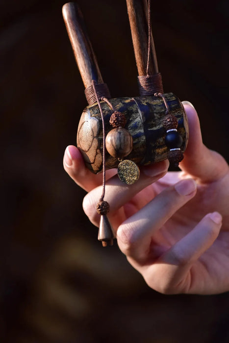 Hand holding a decorative object with intricate designs and a tassel against a dark background