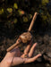 Hand holding a wooden tool with a textured handle against a natural background