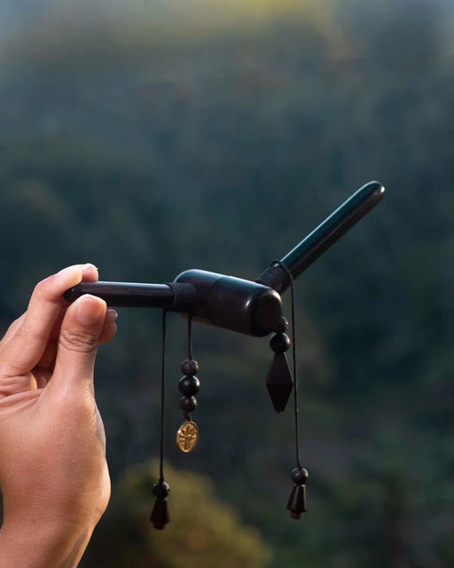 Hand holding a black object with dangling beads against a blurred natural background