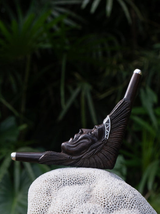 Decorative item resembling a face on a stone surface with a dark green leafy background
