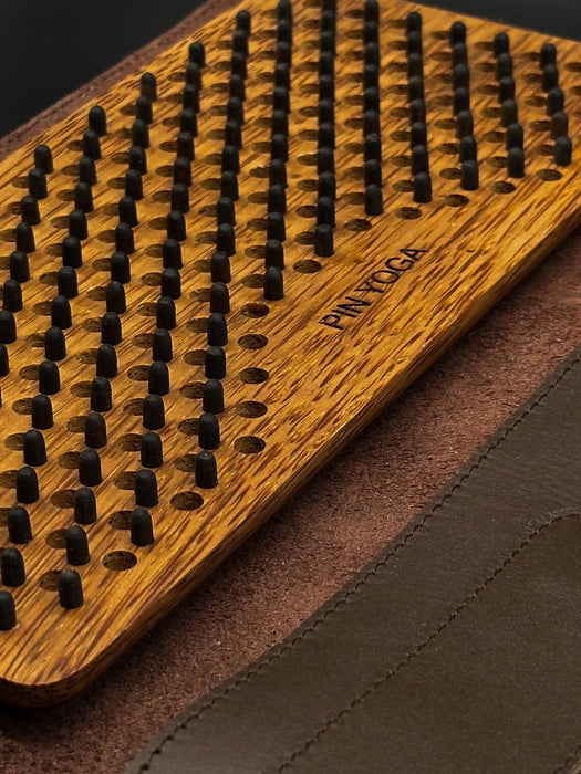 Wooden massage board with textured surface and 'PIN YOGA' branding on a brown mat.