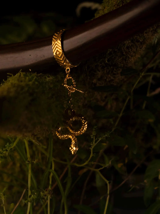 Gold bracelet with a decorative clasp on a wooden surface with greenery