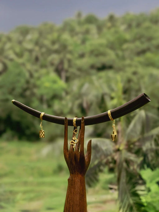 Gold earrings hanging from a wooden branch with a blurred green forest background