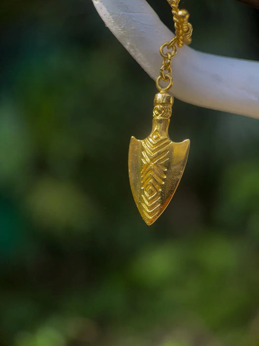 Gold pendant shaped like a traditional weapon on a blurred natural background