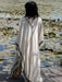 Person wearing a white dress with black patterns standing by a water body with lily pads.