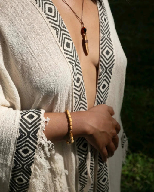 Person wearing a patterned garment with fringe details, holding hands together.